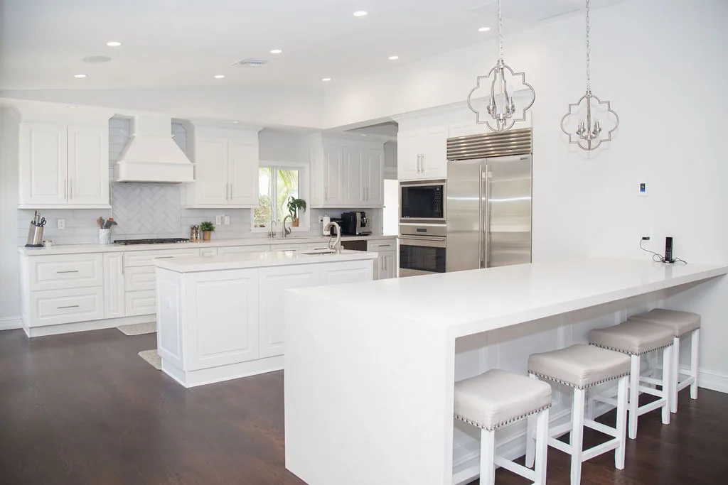 White kitchen with marble backsplash, stainless appliances, and waterfall island.