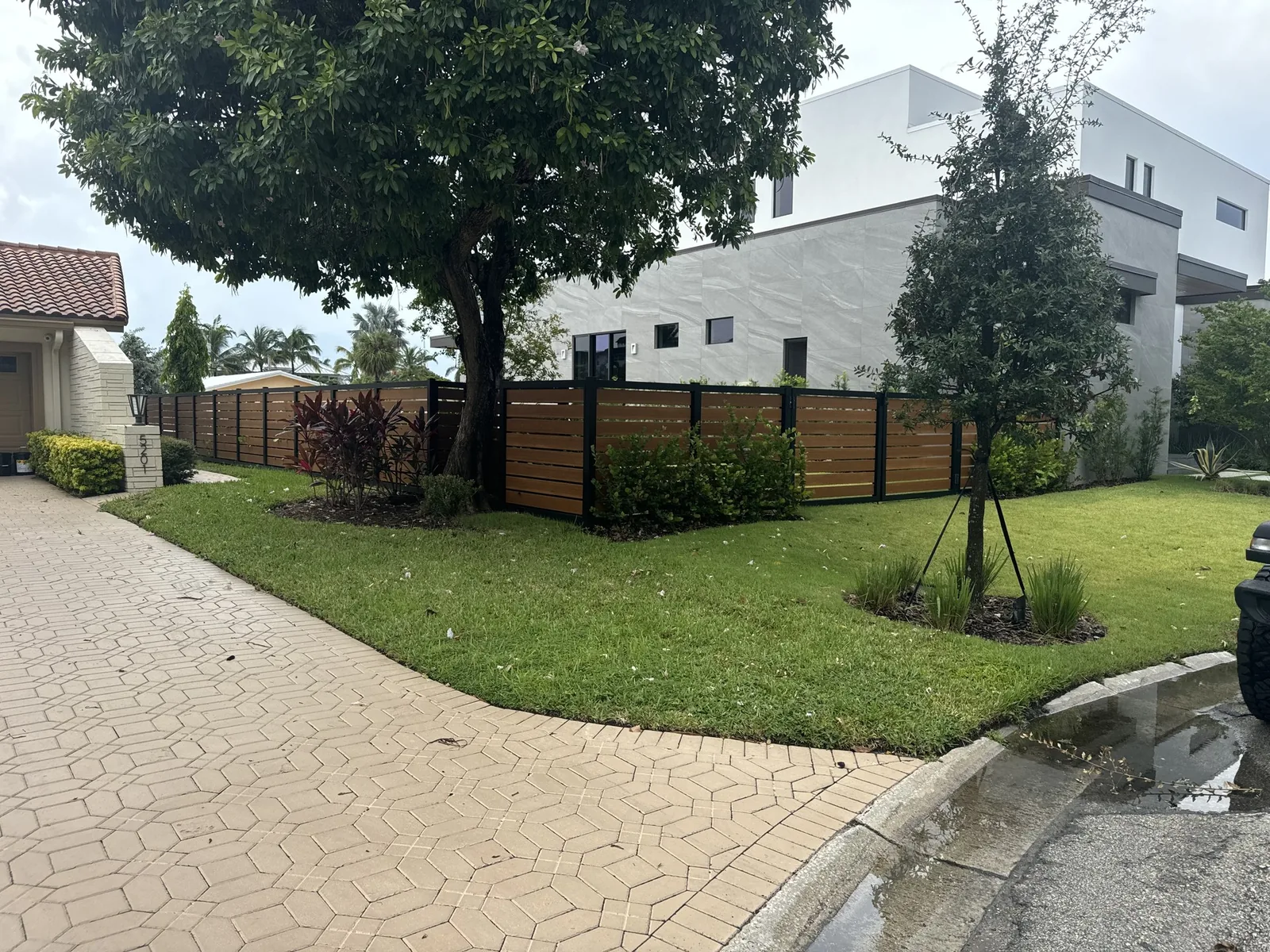 Horizontal wood and metal fence with brick paver driveway design.