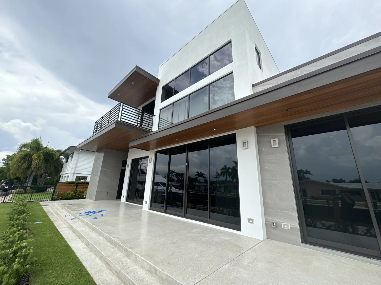 Two-story home with concrete patio, large glass doors, and metal railing.