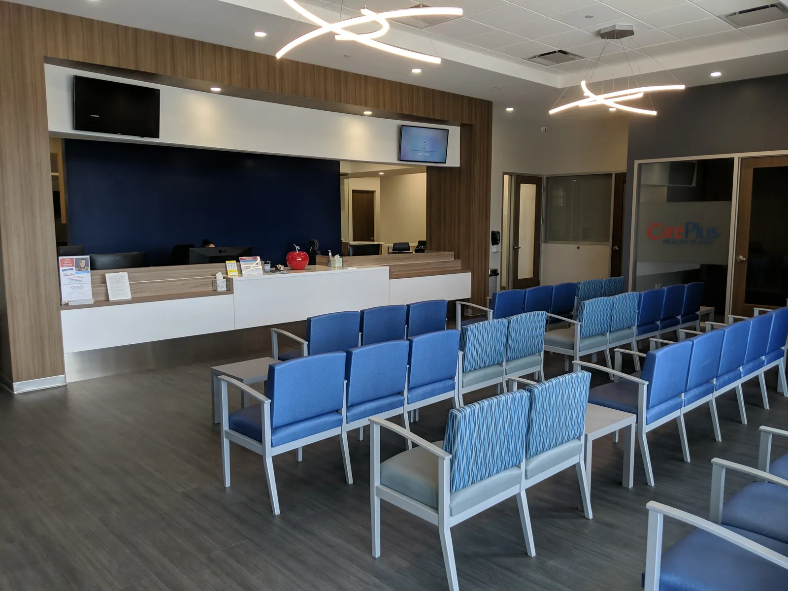 Medical office reception with blue seating, white desk, and wood paneling.