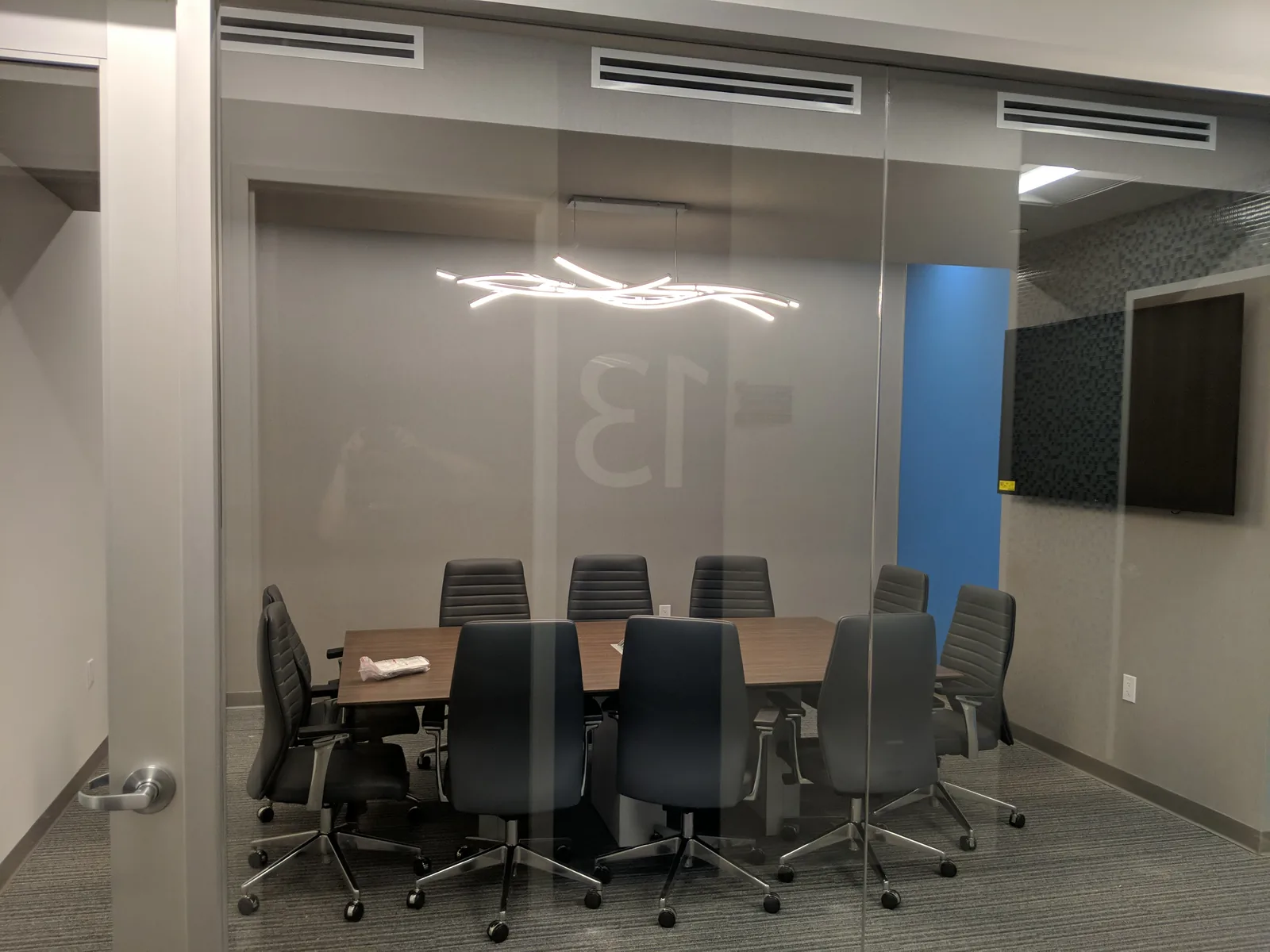 Glass-walled conference room with wooden table and linear pendant lighting.