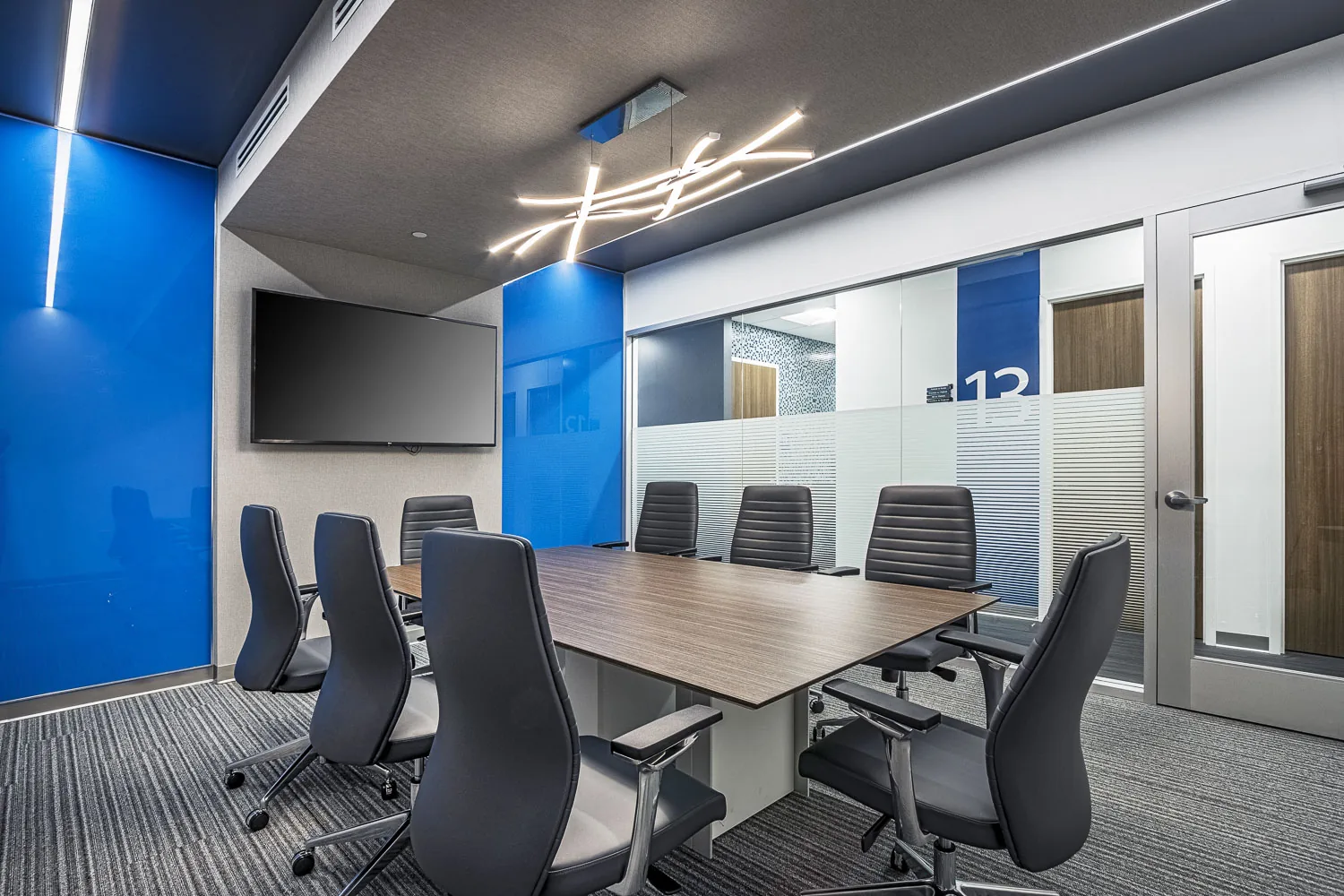 Conference room with wood table, blue accent wall, and glass partitions.