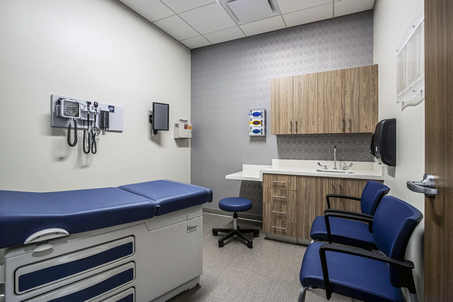 Exam room with blue examination table, wood cabinetry, and support seating.